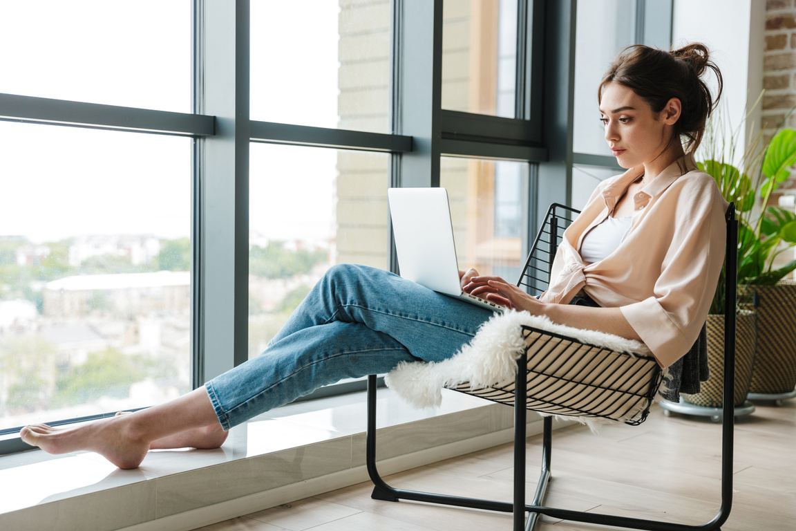 Image of Focused Woman Working with Laptop While Sitting in Armchair